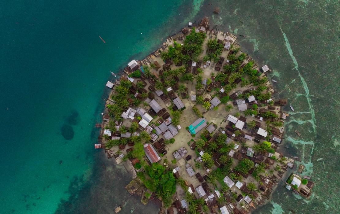 Aerial view of populated circular island with houses, surrounded by blue ocean.